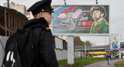 Военный курсант стоит перед билбордом, пропагандирующим контрактную армейскую службу в Санкт-Петербурге, 5 октября 2022 г. /Getty Images