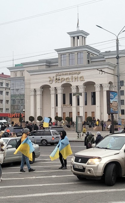 С другой стороны площади — кинотеатр «Украина», бойцы поднимаются на его крышу и под аплодисменты горожан устанавливают еще один флаг. Через два часа — на крыше еще одного здания в центре, теперь площадь с трех сторон в национальных флагах. /Getty Images