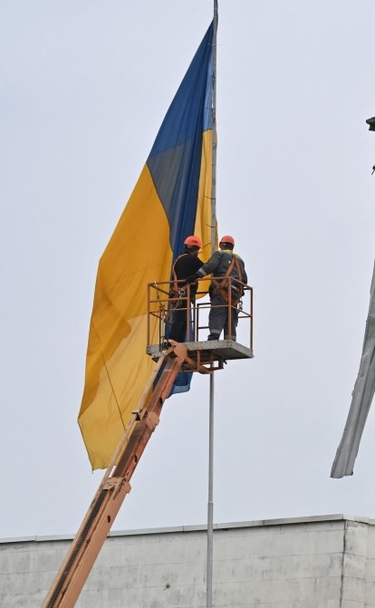 Коммунальщики поднимают украинский флаг возле разрушенного здания в Макарове на Киевщине /Getty Images